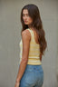 Woman wearing a yellow tank top and blue jeans against a plain background