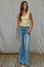 Woman wearing a yellow tank top and blue jeans standing against a plain background