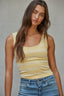 Woman wearing a yellow tank top and blue jeans against a gray background