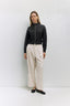 Woman wearing a black top with buttons and beige pants against a white background