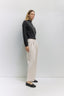 Person wearing a black top with white buttons and beige pants against a white background