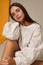 Woman wearing a white textured sweater with puffed sleeves against a neutral background