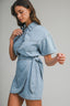 Woman wearing a light blue denim dress against a gray background
