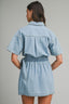 Woman wearing a light blue denim dress against a gray background