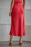 Person wearing a red satin midi skirt with a plain background