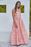 Woman wearing a pink striped dress against a white wall with greenery.
