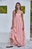 Woman wearing a pink striped dress against a white wall with greenery.