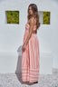 Woman wearing a pink striped dress against a white wall with greenery.