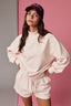 Woman wearing a pink sweatshirt and shorts set with a maroon cap against a pink background
