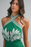 Woman wearing a green and white halter top with leaf patterns on a plain background