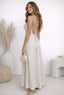 Woman in a white dress standing in a minimalistic room with a vase and plant.