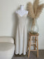 Mannequin wearing a beige dress with a vase of pampas grass on a stool against a white wall.