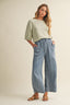 Woman wearing a light green top and blue wide-leg jeans on a beige background