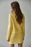 Woman wearing a yellow knitted outfit against a plain background