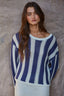 Woman wearing a blue and white striped sweater against a textured wall.
