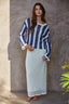 Woman wearing a blue and white striped sweater and white skirt against a textured wall.