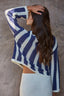 Woman wearing a blue and white patterned crochet sweater against a gray background