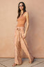 Woman wearing a brown tank top and patterned pants against a beige wall.