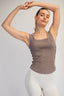 Woman wearing a brown tank top and white pants against a plain background