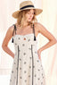 Woman wearing a white dress with black floral patterns and a straw hat with a black band.