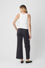 Woman wearing a white sleeveless top and dark pants on a white background