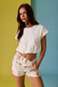 Woman wearing a white top and floral shorts against a colorful background