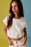 Woman wearing a white top and floral pants against a multicolored background
