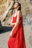 Woman in a red maxi dress standing on a beach with rocks in the background