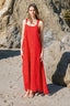 Woman in a red maxi dress standing on a rocky beach.