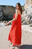 Woman in a red maxi dress standing on a rocky beach.