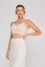 Woman wearing a beige lace top and white skirt on a plain background