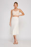 Woman wearing a beige top and white skirt on a plain background