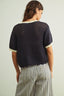 Person wearing a dark knit top with light trim on a plain background