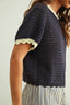 Person wearing a navy blue knitted top with white trim on a plain background