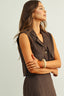 Woman wearing a brown sleeveless jacket and skirt set against a plain background