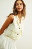 Woman wearing a light-colored vest over a white outfit on a plain background