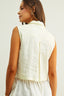 Woman wearing a light-colored vest over a white dress against a plain background