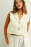 Woman wearing a light-colored sleeveless top and pants against a plain background