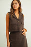 Woman wearing a brown sleeveless vest over a matching dress against a plain background