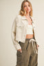 Woman wearing a light-colored denim jacket over a white crop top and olive green pants on a beige background