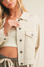 Woman wearing a light-colored denim jacket over a ribbed top with a neutral background