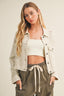 Woman wearing a light-colored jacket over a white crop top and olive green pants on a plain background