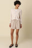Woman wearing a light-colored cardigan and striped shorts on a beige background
