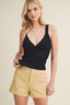 Woman wearing a black sleeveless top and beige shorts on a beige background