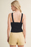 Woman wearing a black sleeveless top and beige shorts on a beige background