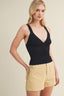 Woman wearing a black tank top and beige shorts on a beige background