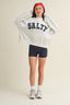 Person wearing a white sweatshirt with 'SALTY' text, black shorts, and white sneakers on a beige background