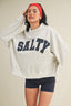 Woman wearing a gray sweatshirt with 'SALTY' printed on it, black shorts, and a red headband against a beige background.