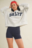Person wearing a white sweatshirt with 'SALTY' text and black shorts on a beige background