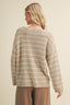 Woman wearing a beige and white striped sweater against a plain background